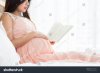 pregnant-woman-in-pink-dress-reading-a-book-on-the-bed-in-bedroom-787188685.jpg