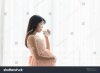 pregnant-woman-in-beautiful-pink-dress-drinking-milk-in-bedroom-780632272.jpg