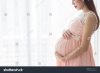 pregnant-woman-in-beautiful-pink-dress-standing-close-up-a-window-in-her-bedroom-782830618.jpg
